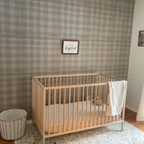 Airy baby room with crib, white blanket, toys, "long live boyhood" frame, rattan light, and gingham wallpaper.