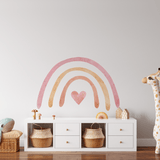A children's playroom with a pastel rainbow wall sticker above a white dresser. The room has a whimsical feel with a large plush dolphin toy on a wicker bench, a giraffe-shaped toy, and woven baskets for storage.