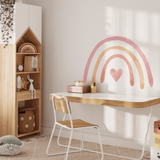 A bright and airy homeschool or study room for a child with a pastel rainbow wall decal. This room features a wooden bookshelf filled with supplies, a minimalist desk with a white chair, and playful elements like a stuffed octopus toy and colorful storage boxes.