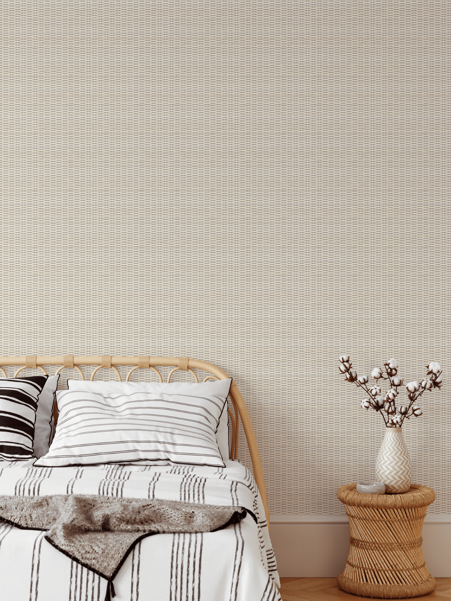 A warm and inviting bedroom showcasing white-washed rattan weave wallpaper, a rattan bed frame with striped bedding, and a vase of cotton stems on a woven bedside stool.