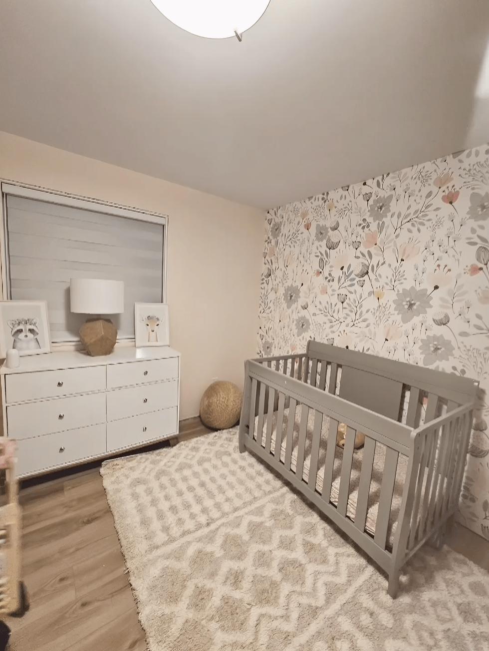 Nursery room with floral wallpaper, crib, dresser, and textured rug after decoration.