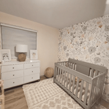 Nursery room with floral wallpaper, crib, dresser, and textured rug after decoration.