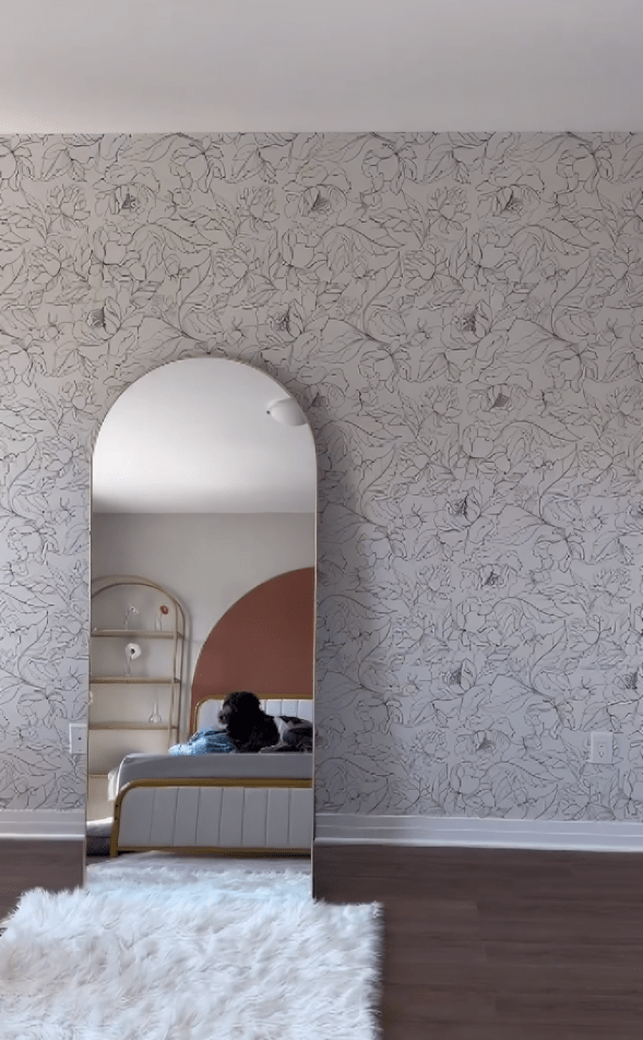 "Modern bedroom with neutral wildflower wallpaper, arch mirror, and white fluffy rug