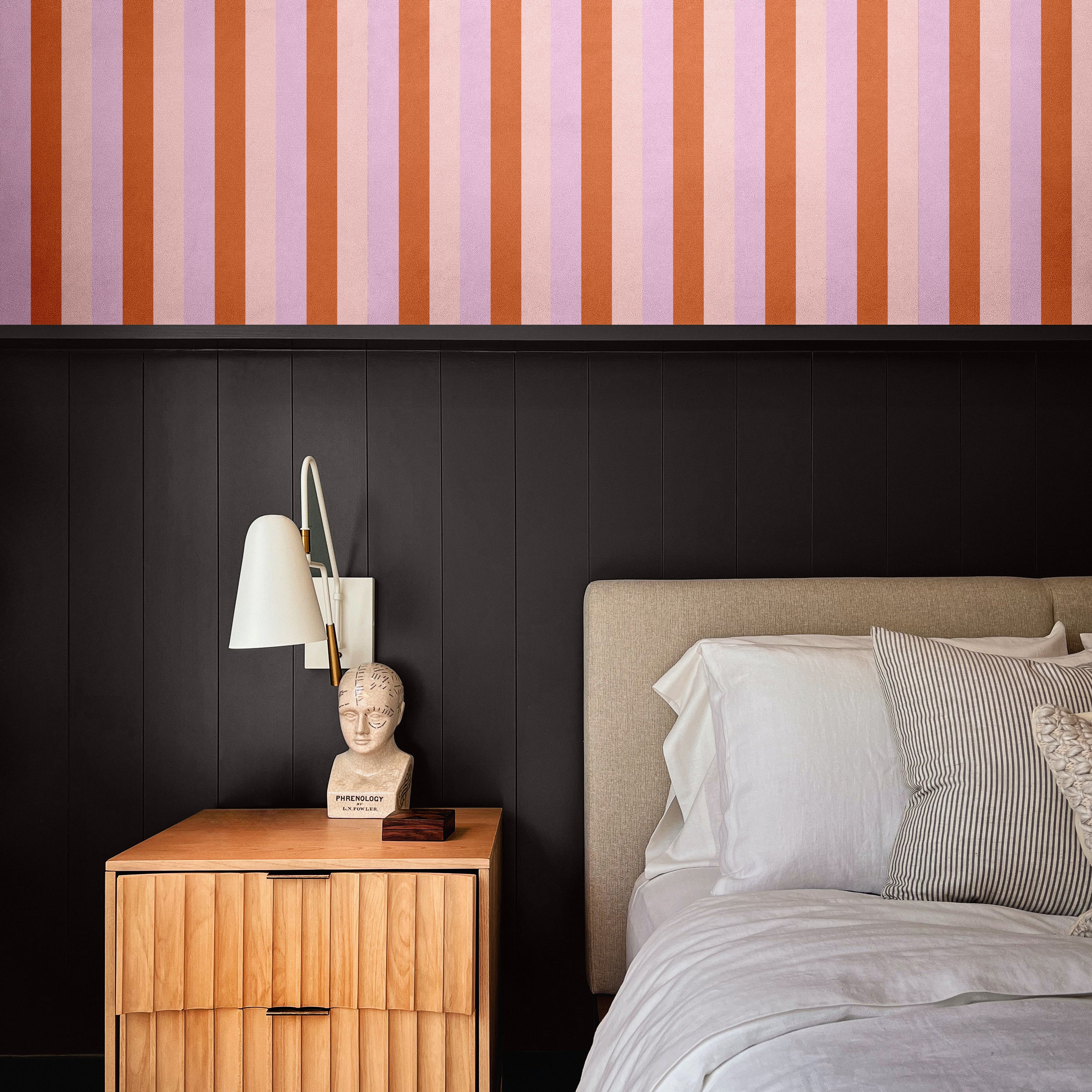 Moody modern bedroom with half-wall Taffy wallpaper above black paneling