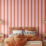 Taffy striped wallpaper in warm-toned bedroom with cane pendants and rust bedding