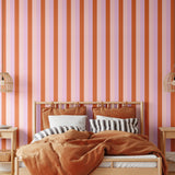 Taffy striped wallpaper in warm-toned bedroom with cane pendants and rust bedding