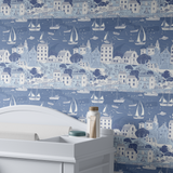Sailboat harbor wallpaper behind white nursery dresser with sailboats and seaside village pattern