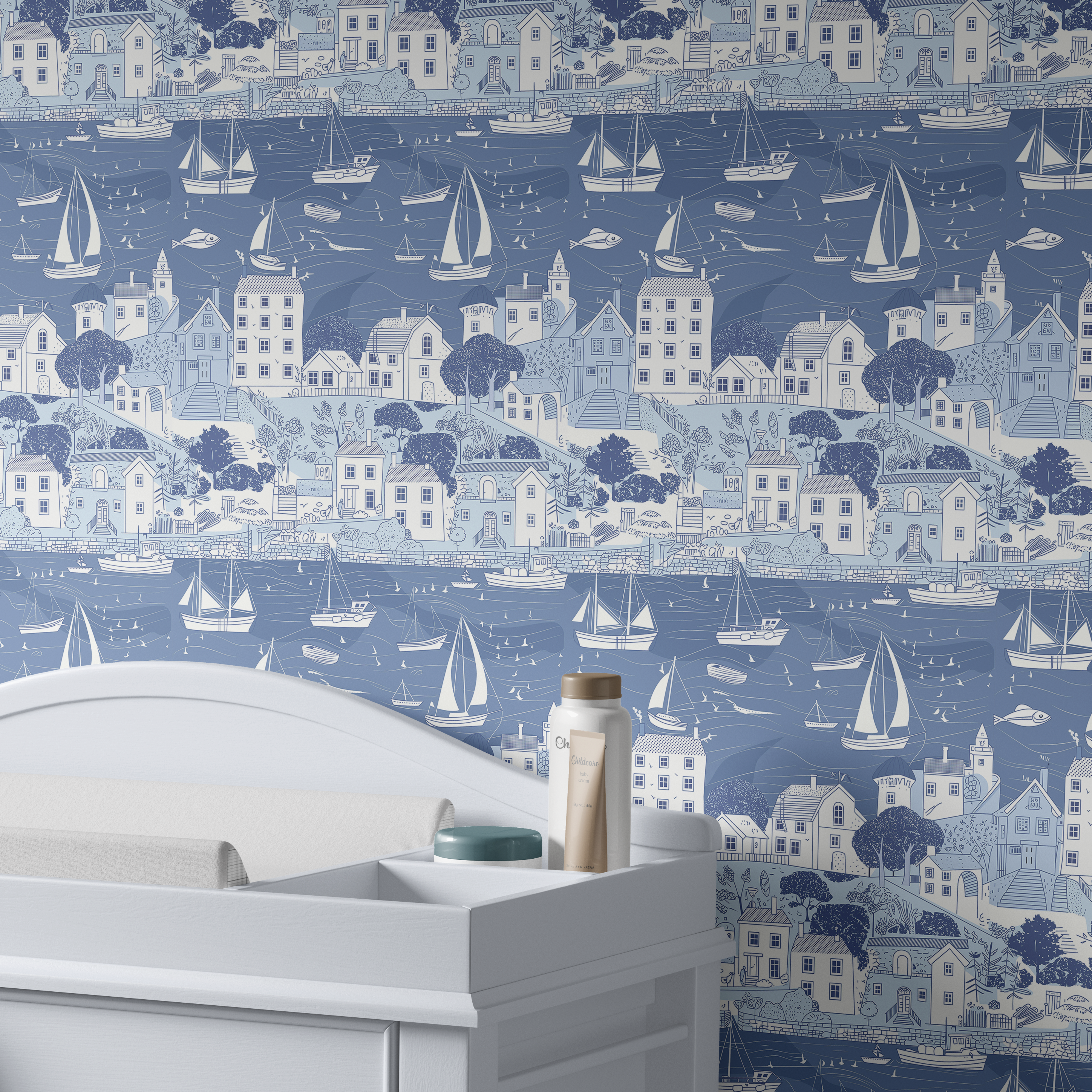Sailboat harbor wallpaper behind white nursery dresser with sailboats and seaside village pattern