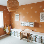 Bright and educational playroom featuring terracotta walls with white sunburst decals, wooden furniture, and storage units