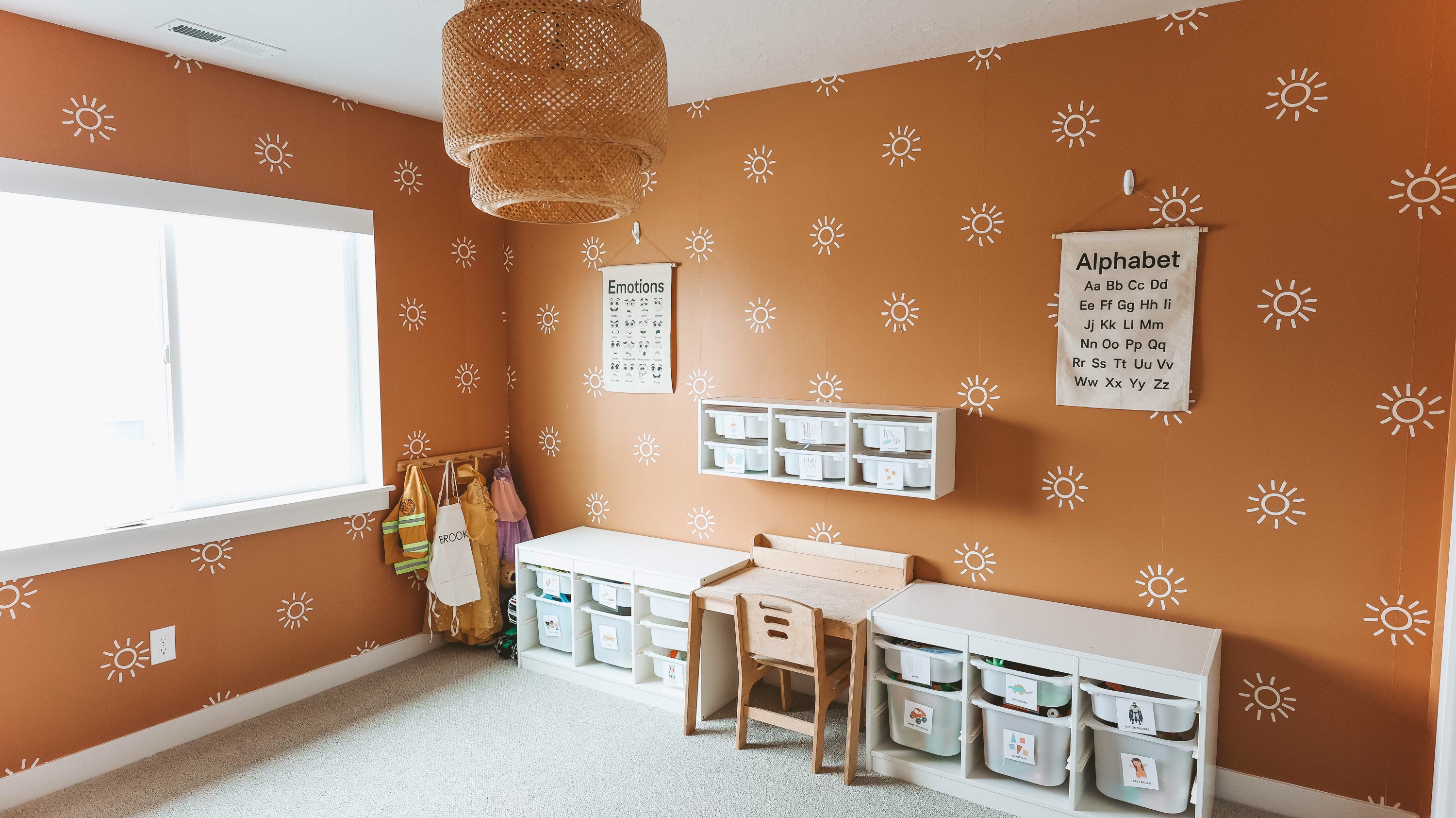 Bright and educational playroom featuring terracotta walls with white sunburst decals, wooden furniture, and storage units