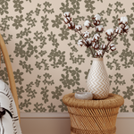 Vase with cotton branches on a woven stool against floral wallpaper