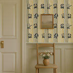 Whimsical cats and dogs wallpaper on striped background in beige and mustard tones, styled in a cozy room with chair and flowers.
