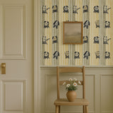 Whimsical cats and dogs wallpaper on striped background in beige and mustard tones, styled in a cozy room with chair and flowers.