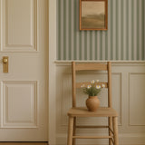Cozy entryway with sage green striped wallpaper and wooden chair with vase of daisies