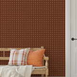 Warm brown grid wallpaper behind a rustic wood bench with orange and plaid pillows
