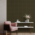Dark green fine-line grid plaid wallpaper behind pink accent chair and modern console table
