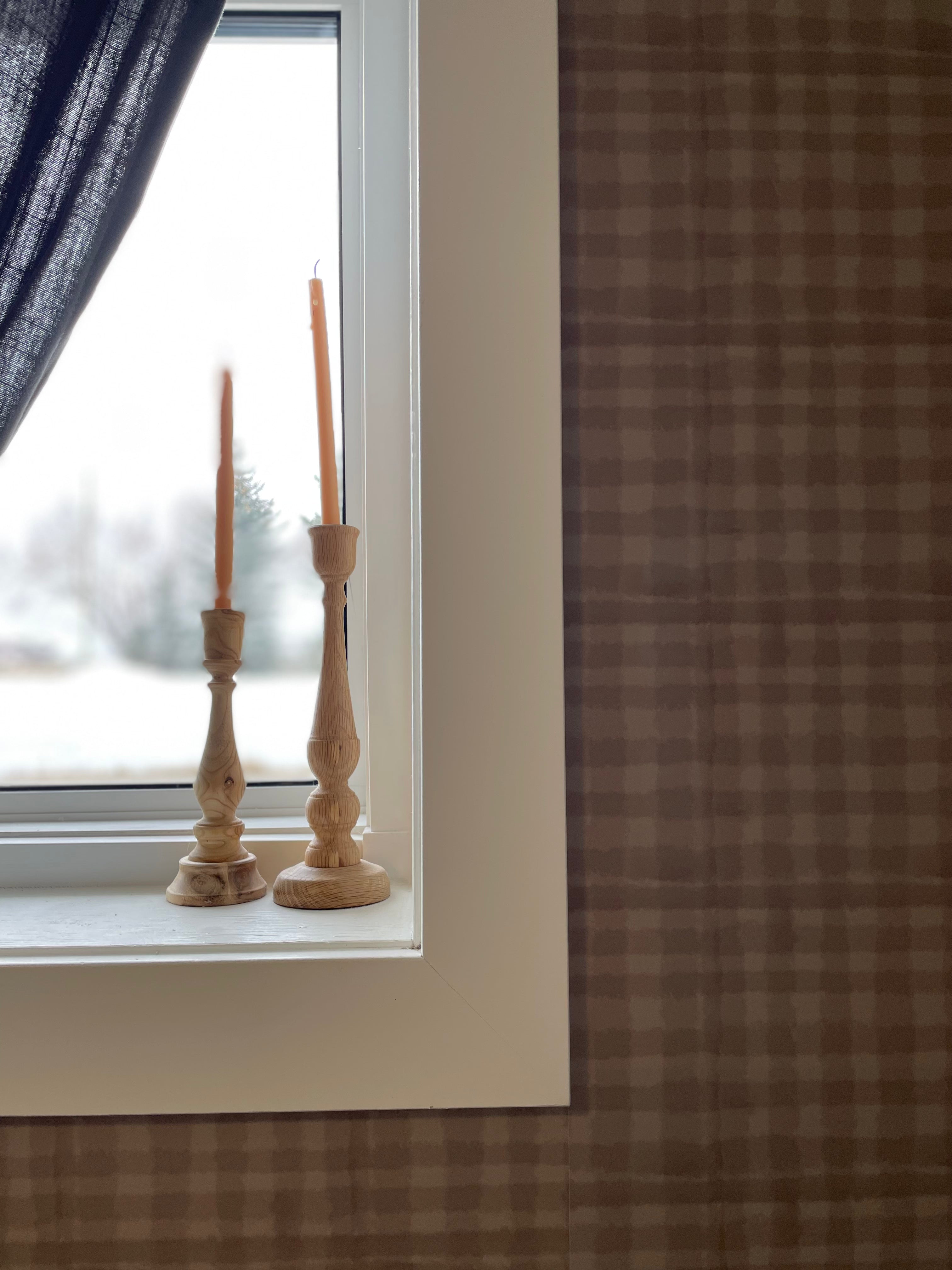 Minimalistic décor with wooden candlesticks on a windowsill, complemented by mini plaid wallpaper, creating a serene ambiance.