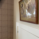 A painting of two dogs running in a field, displayed against a mini plaid wallpaper in a cozy room corner