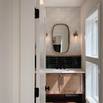 View through doorway showing beige zellige tile wallpaper above bathroom vanity with mirror and moody green tile contrast