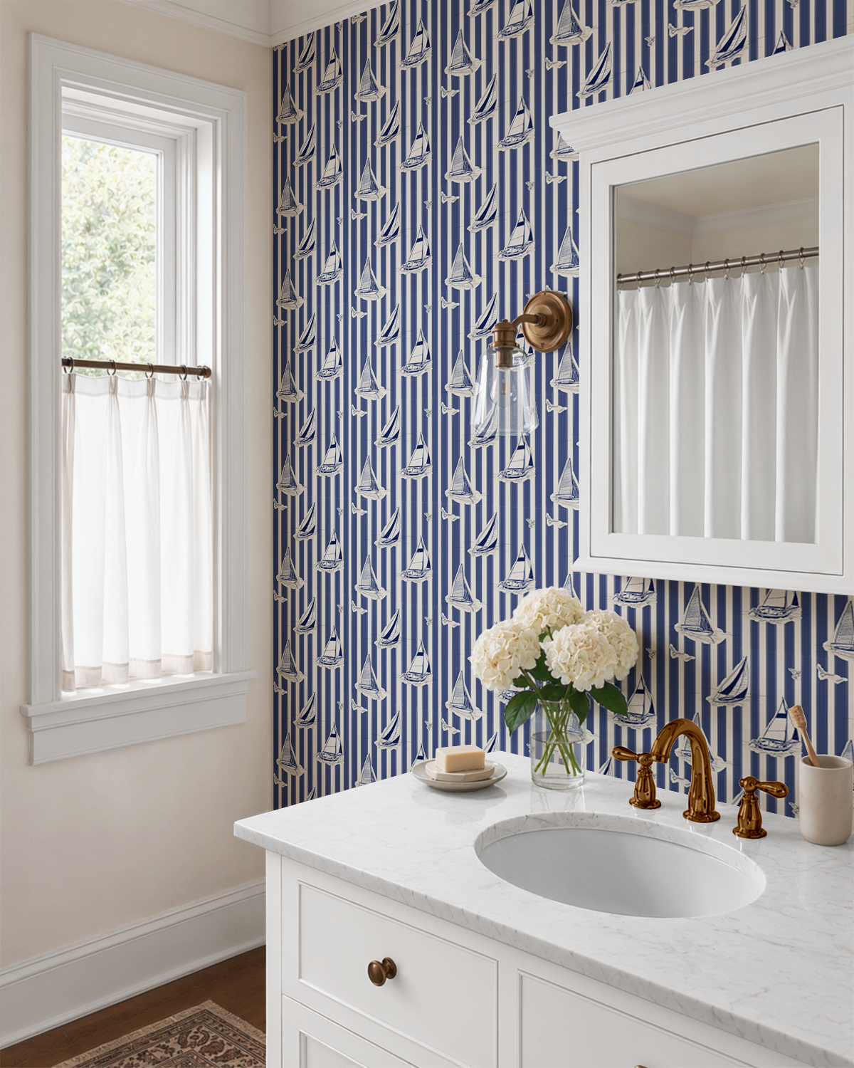 Blue and cream sailboat wallpaper styled in a traditional bathroom with white vanity and brass fixtures