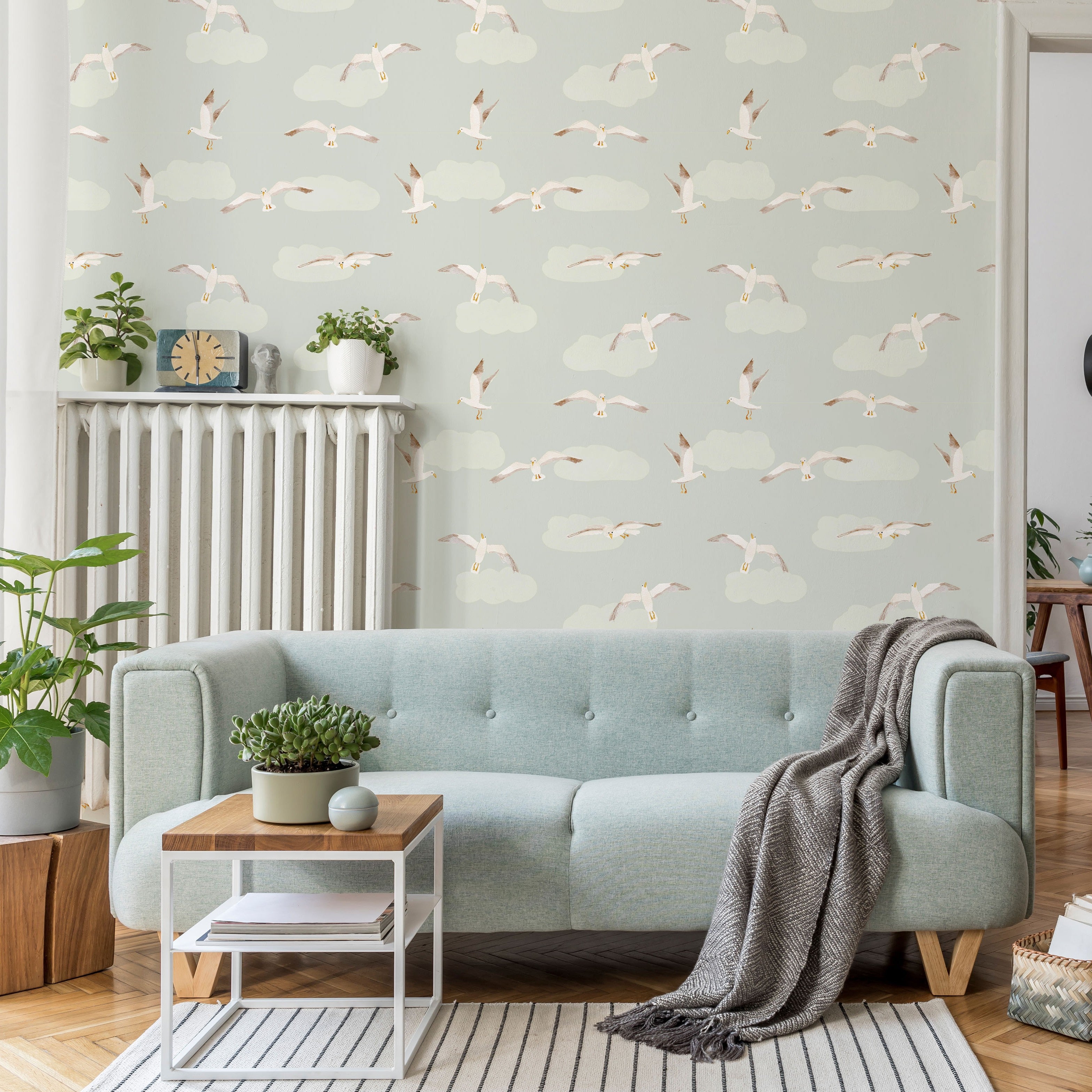 Living room with light blue sofa, wooden side table, and blue wallpaper with flying seagull pattern.