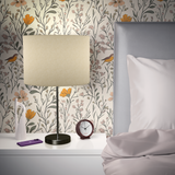 Nightstand with lamp and clock in front of Songbird Meadow wallpaper