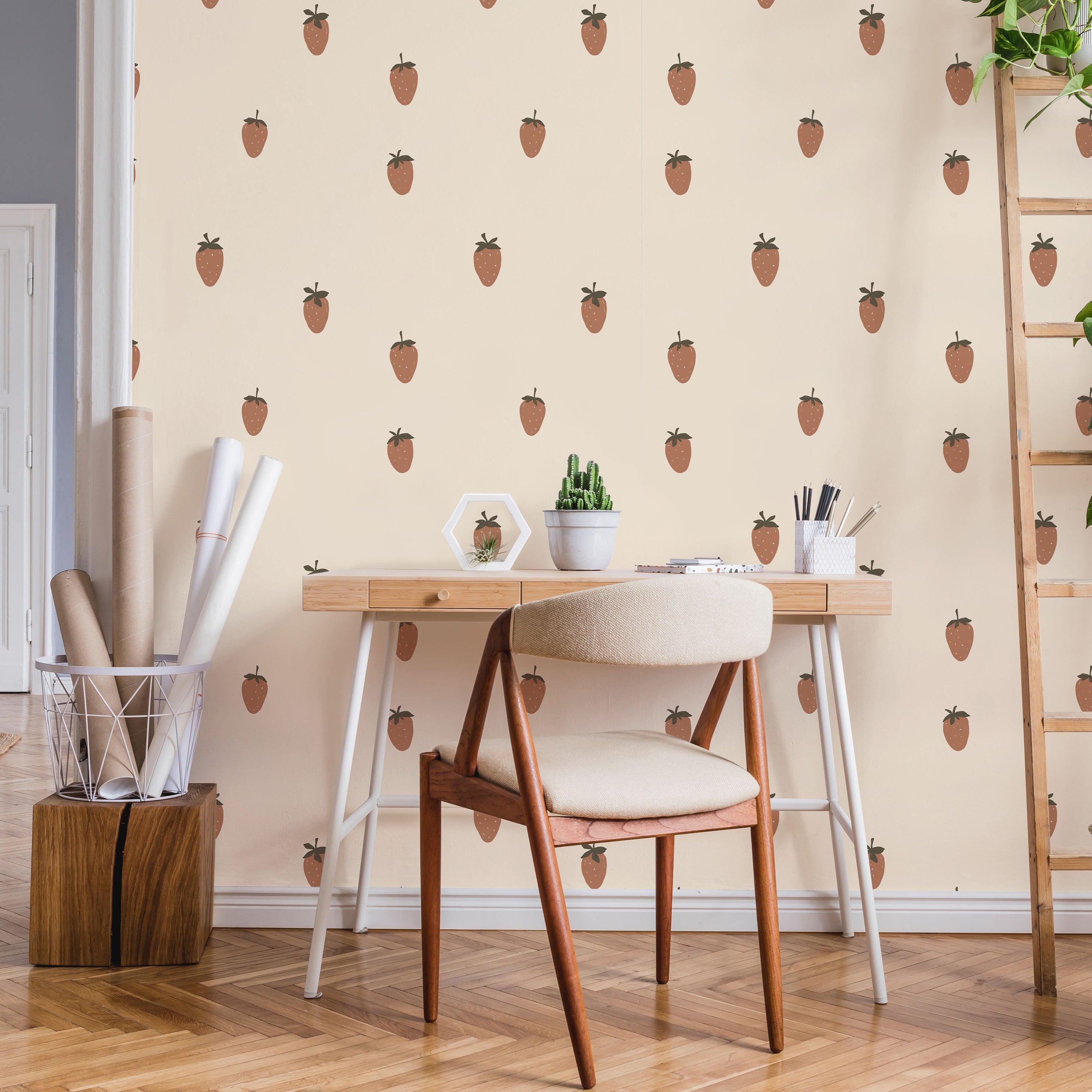 Wooden desk, chair, and decor against a wall with strawberry pattern wallpaper.