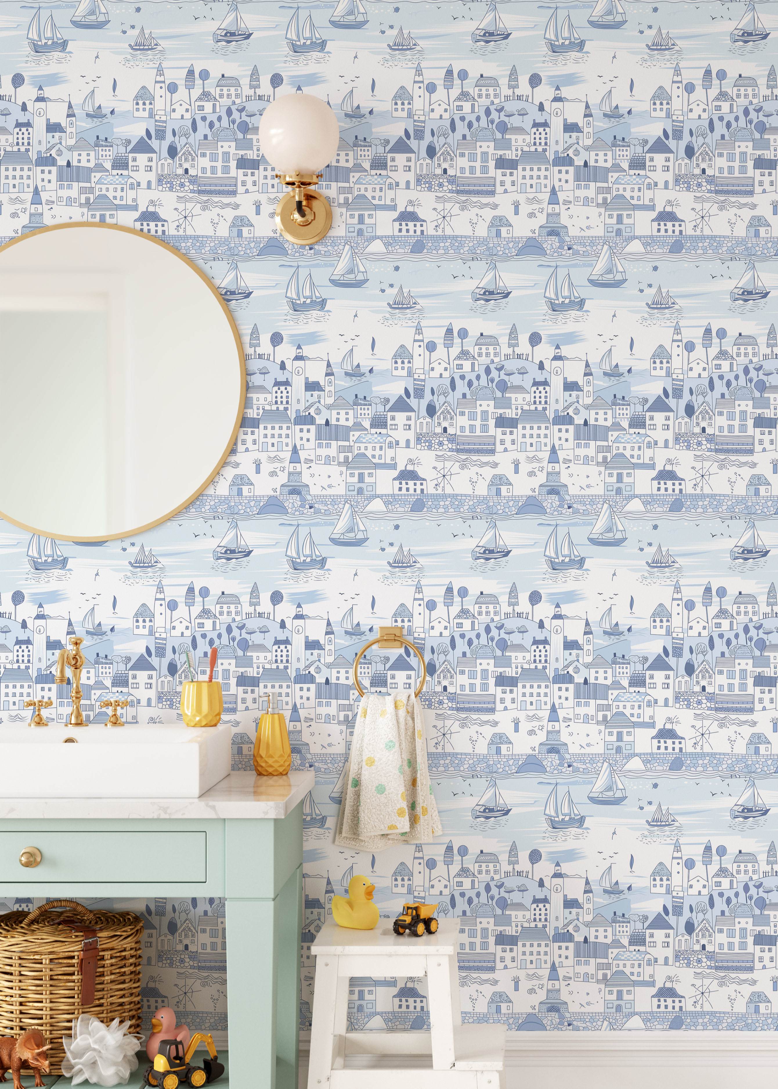 Light blue coastal village wallpaper with sailboats styled in a kids bathroom featuring mint vanity and gold fixtures