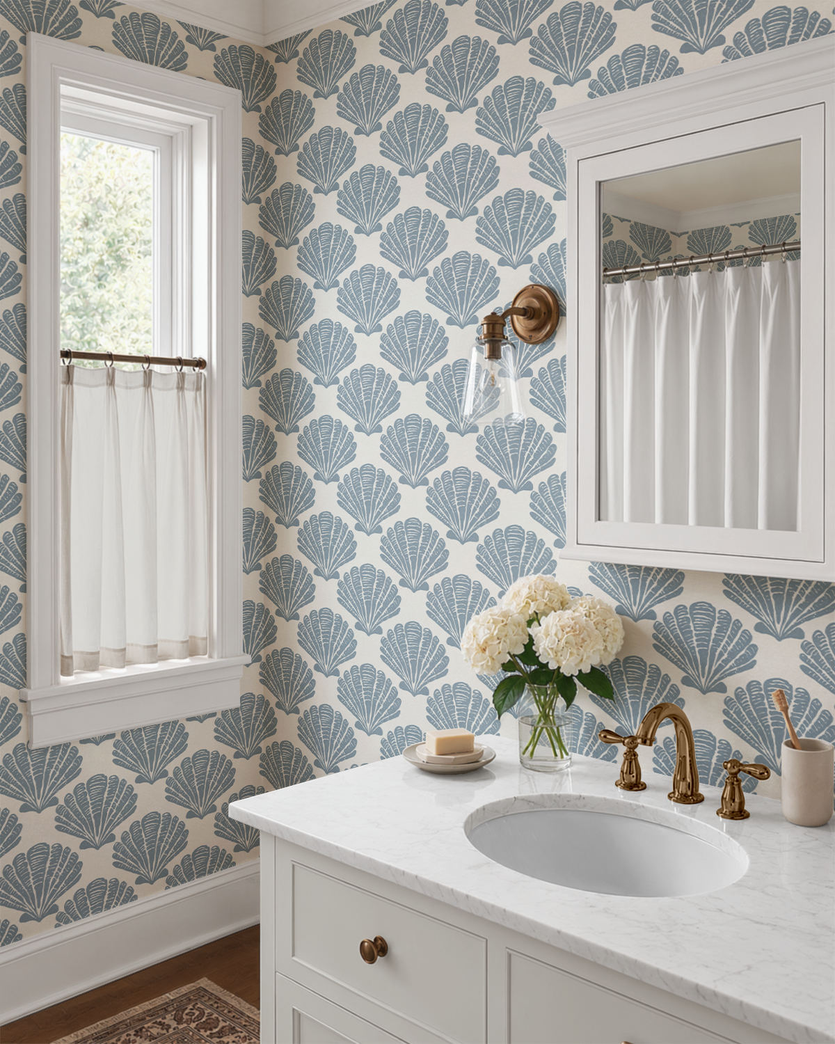 Blue Tidepool Shell wallpaper in a bright coastal bathroom with brass fixtures, marble vanity, and repeating seashell pattern.