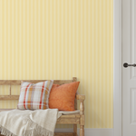 Yellow striped wallpaper in an entryway with rustic wooden bench and orange pillows.
