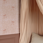 Elegant blush bedroom wall with Pink Bow Vintage Wallpaper, draped canopy curtains, and mauve panel molding.