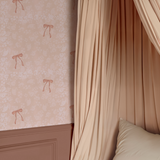 Elegant blush bedroom wall with Pink Bow Vintage Wallpaper, draped canopy curtains, and mauve panel molding.