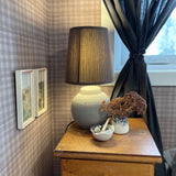 A vintage styled room featuring a lamp, dried flowers, and framed pictures, with mini plaid wallpaper adding texture to the space.