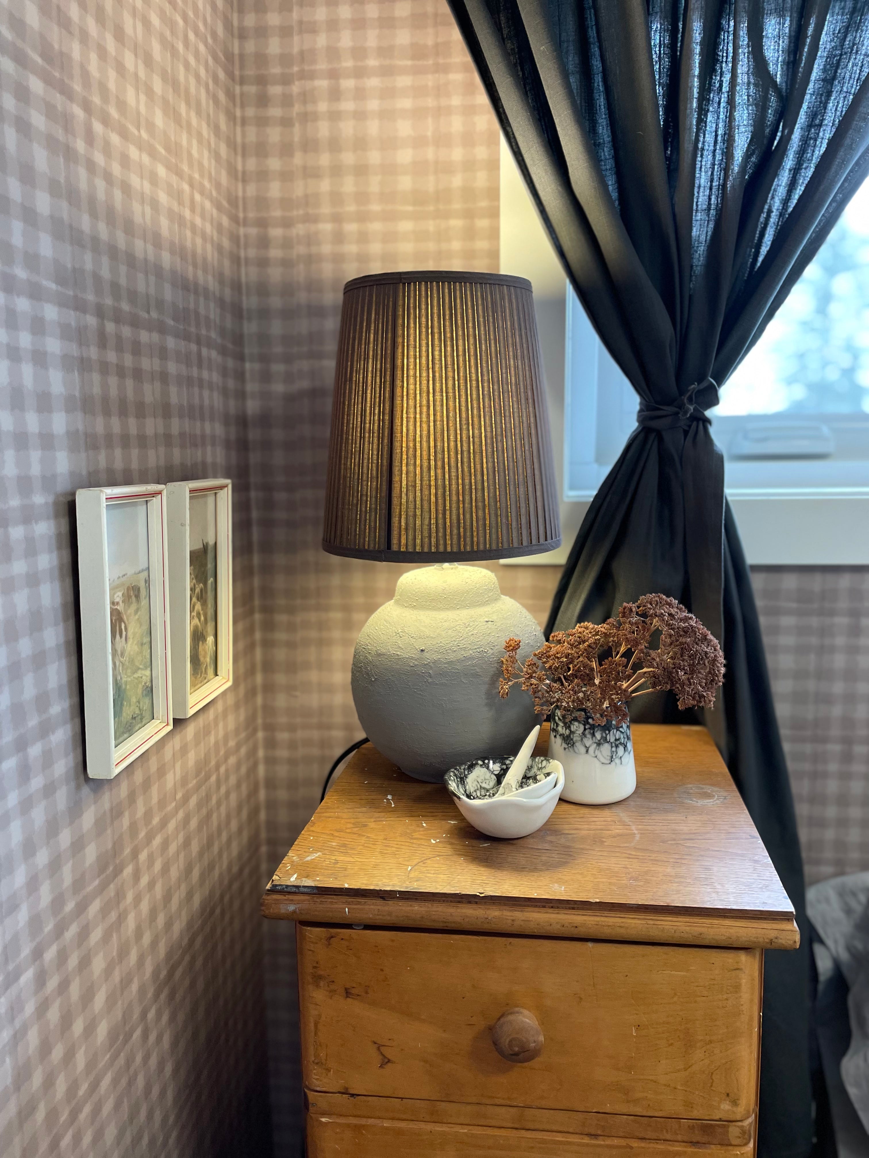 A vintage styled room featuring a lamp, dried flowers, and framed pictures, with mini plaid wallpaper adding texture to the space.