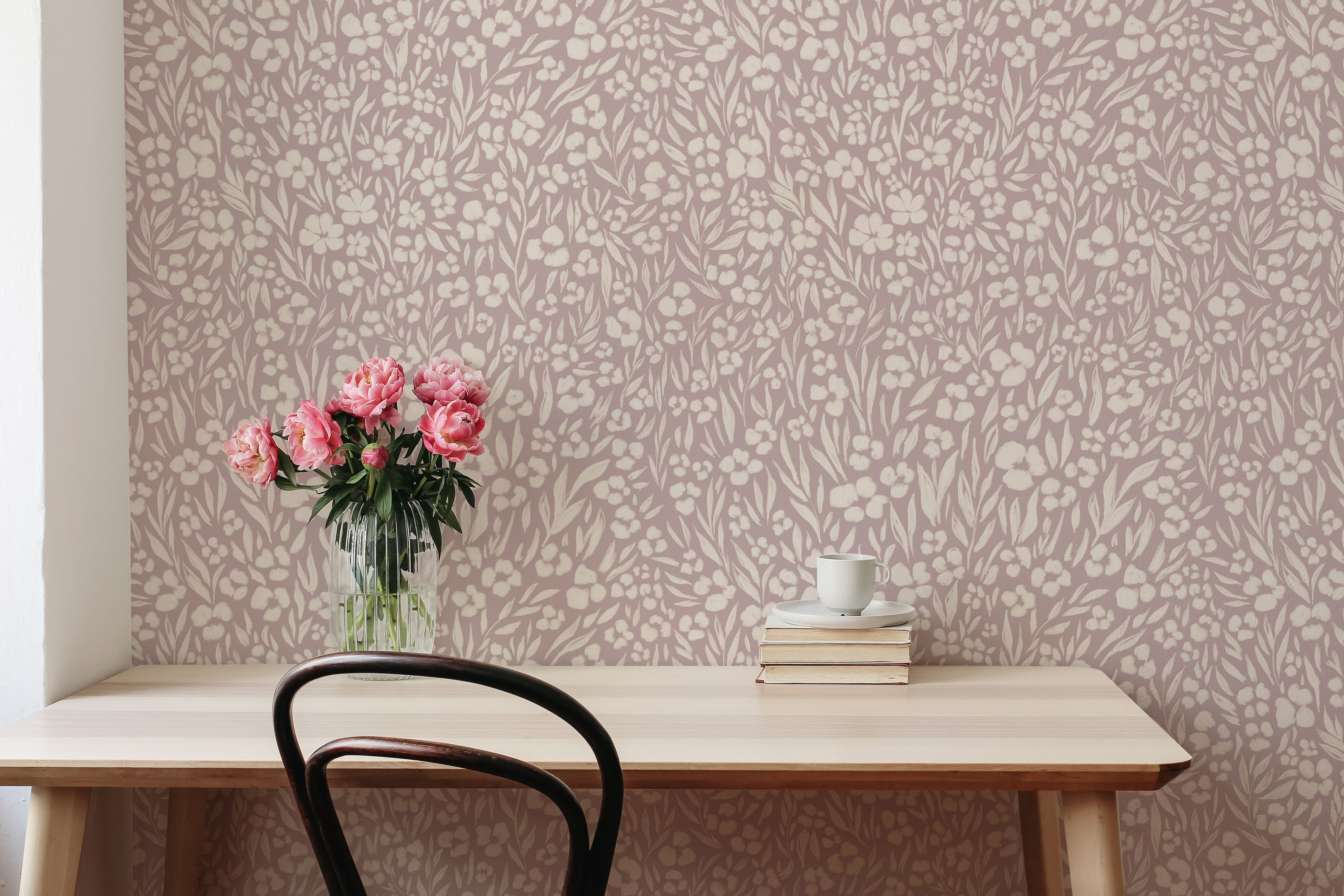 Desk with flowers and books against a floral wallpapered wall