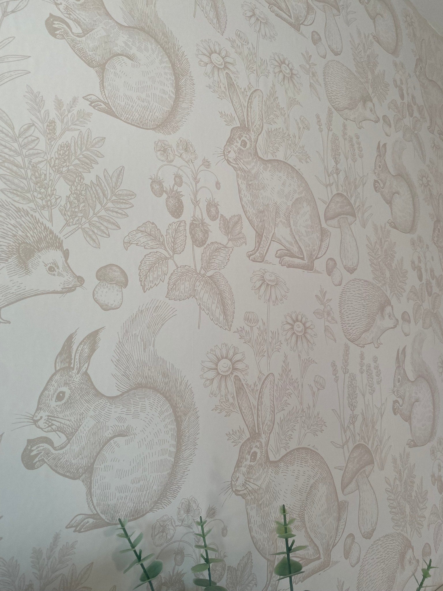 Close-up of a neutral nursery wallpaper depicting various woodland animals like rabbits and squirrels in a detailed beige sketch style.