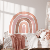 A cozy girls' bedroom with an Autumn Rainbow wall decal above the bed. The room features a soft pink blanket, white metal bed frame, and a dreamy canopy, creating a warm and inviting space.