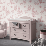 Pink Ballerina Toile Wallpaper in a nursery with a pink changing table and plush chair