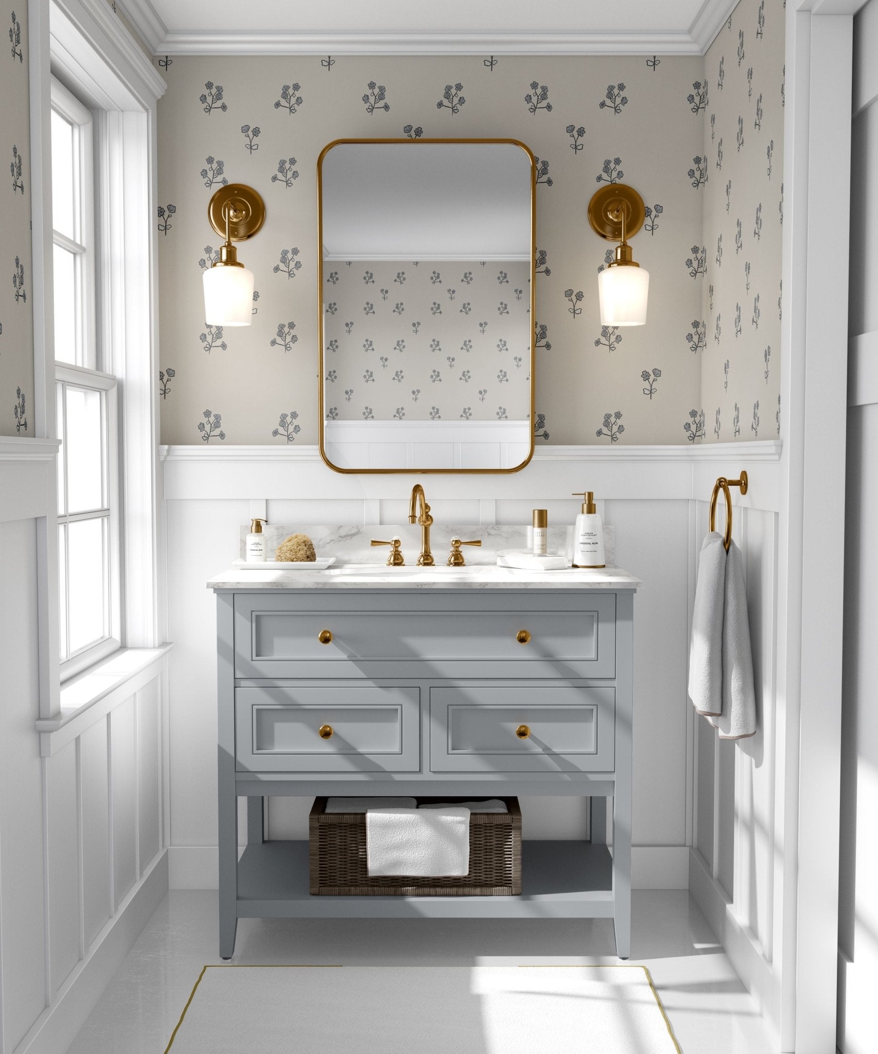 A bright bathroom with walls covered in bluebell flower wallpaper matching the previous image. The room features a light blue vanity with golden knobs, a marble top, golden faucets, and a large mirror with a golden frame.