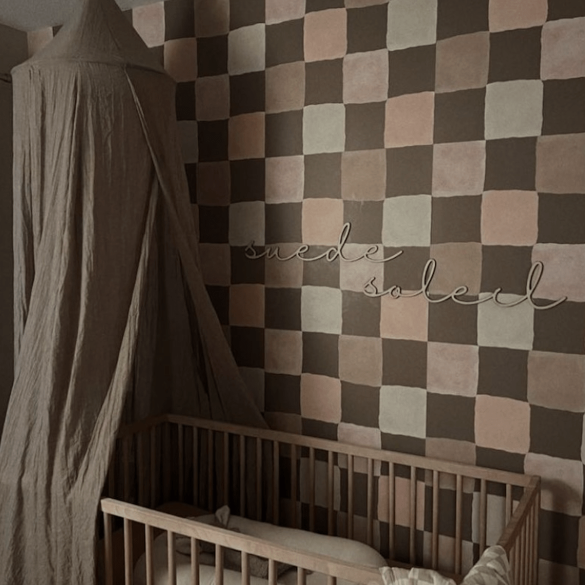 Stylish boho baby nursery featuring a checkered wallpaper in brown and blush pink tones, with a wooden crib, soft bedding, and a canopy, creating a cozy and elegant space