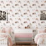 A shared bedroom setup featuring two white metal beds with pink bedding, a pastel-colored dresser, and cowgirl-themed wallpaper decorated with scenes of cowgirls and horses, creating a playful and inviting atmosphere.