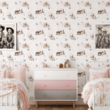 A shared bedroom setup featuring two white metal beds with pink bedding, a pastel-colored dresser, and cowgirl-themed wallpaper decorated with scenes of cowgirls and horses, creating a playful and inviting atmosphere.