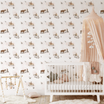 A charming nursery with a white crib, pastel-colored accessories, and cowgirl-themed wallpaper adorned with illustrations of cowgirls, horses, and flowers on a light background.