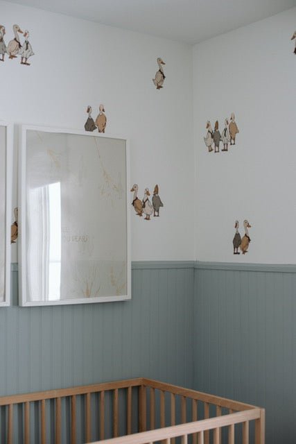 Beautiful nursery with blue wainscotting, and duck/geese decals placed above on white wall.
