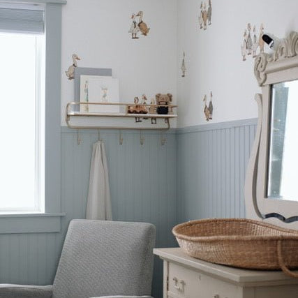 Beautiful nursery with blue wainscotting, and duck/geese decals placed above on white wall.