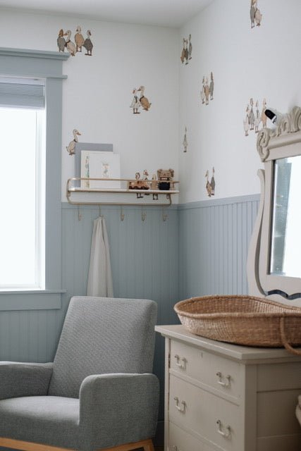 Beautiful nursery with blue wainscotting, and duck/geese decals placed above on white wall.