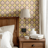 A wooden bedside table with neutral bedding styled against mustard yellow floral scalloped wallpaper, enhancing a rustic bedroom vibe.