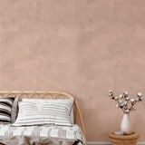 Earthy pink limewash wallpaper in a boho-inspired bedroom with woven furniture and neutral bedding for a soft, calming ambiance