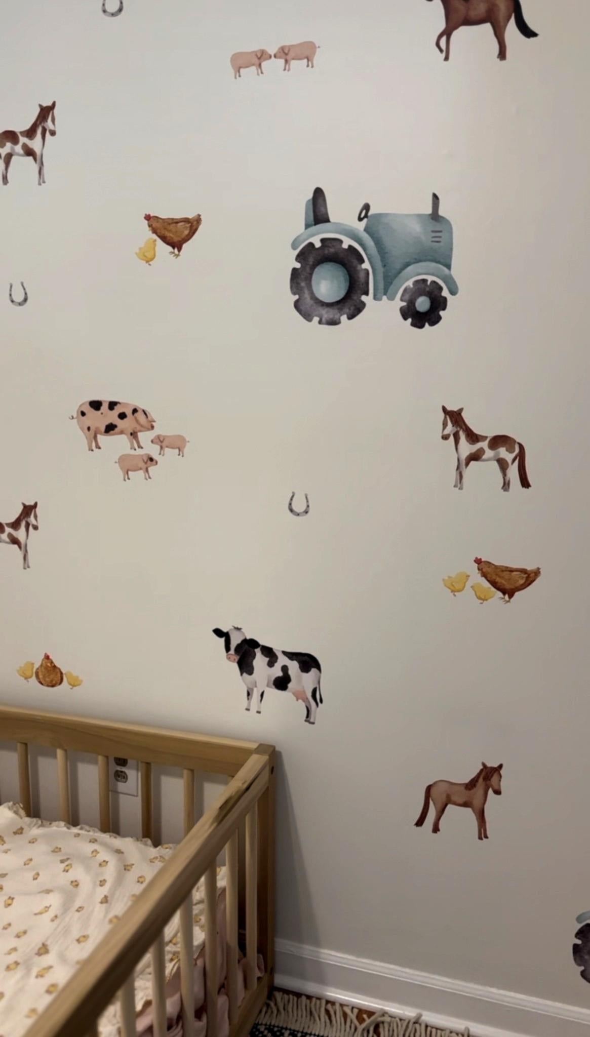 Close-up of a nursery wall decorated with farm animal decals, including a tractor, horses, cows, and chickens. A wooden toddler bed is partially visible, adding to the room's rustic charm