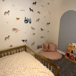 Nursery room corner with a toddler bed, featuring farm animal-themed wallpaper and a cozy reading nook. The wall is decorated with horse, cow, and chicken decals, complemented by a soft pink floor pillow